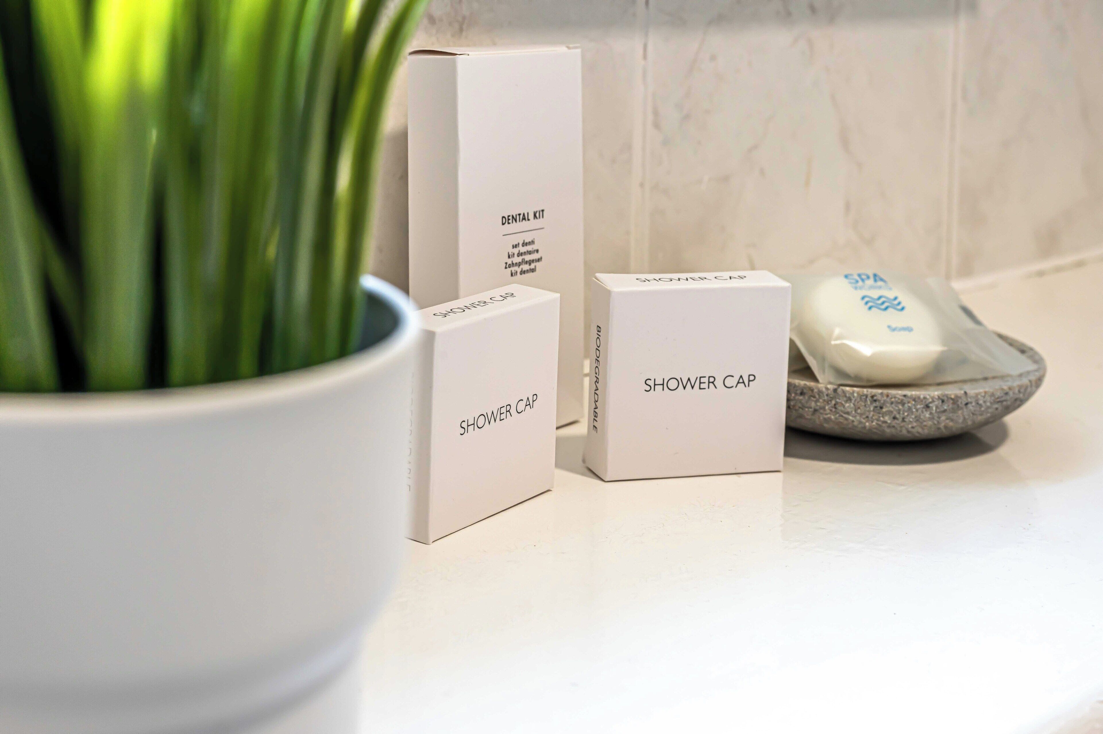 A bathroom with a shower cap, a dental kit, and a spa soap on a countertop.