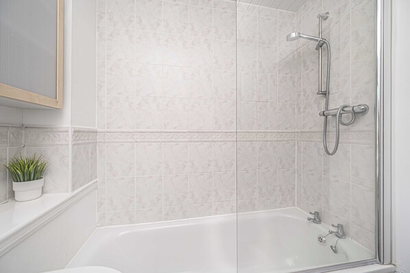 A modern bathroom with a glass-enclosed shower, a white bathtub, and a small potted plant on the windowsill.
