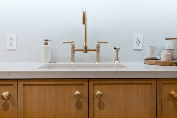 Una cocina moderna con encimera de mármol blanco, grifo dorado y armarios de madera.