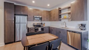 A modern kitchen with dark wood cabinets, stainless steel appliances, a dining table with chairs, and a coffee maker. - TWO Luxe CozySuites in Downtown Cincy (Cincinnati)