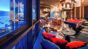 A modern hotel lobby with a pool table, seating area, and a view of the water outside.