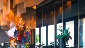 A modern dining area with a marble countertop, two large flower arrangements, and a view of the outdoors through large windows.