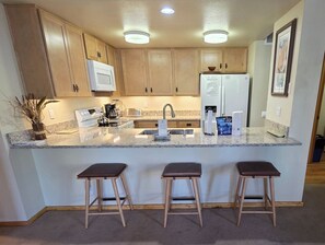 A modern kitchen with wooden cabinets, a white refrigerator, a built-in oven, a sink, and three bar stools.