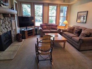 A cozy living room with a fireplace, a television, a sofa, a coffee table, and a chair. - Snowcreek Resort Vacation Rental 879 (Mammoth Lakes)