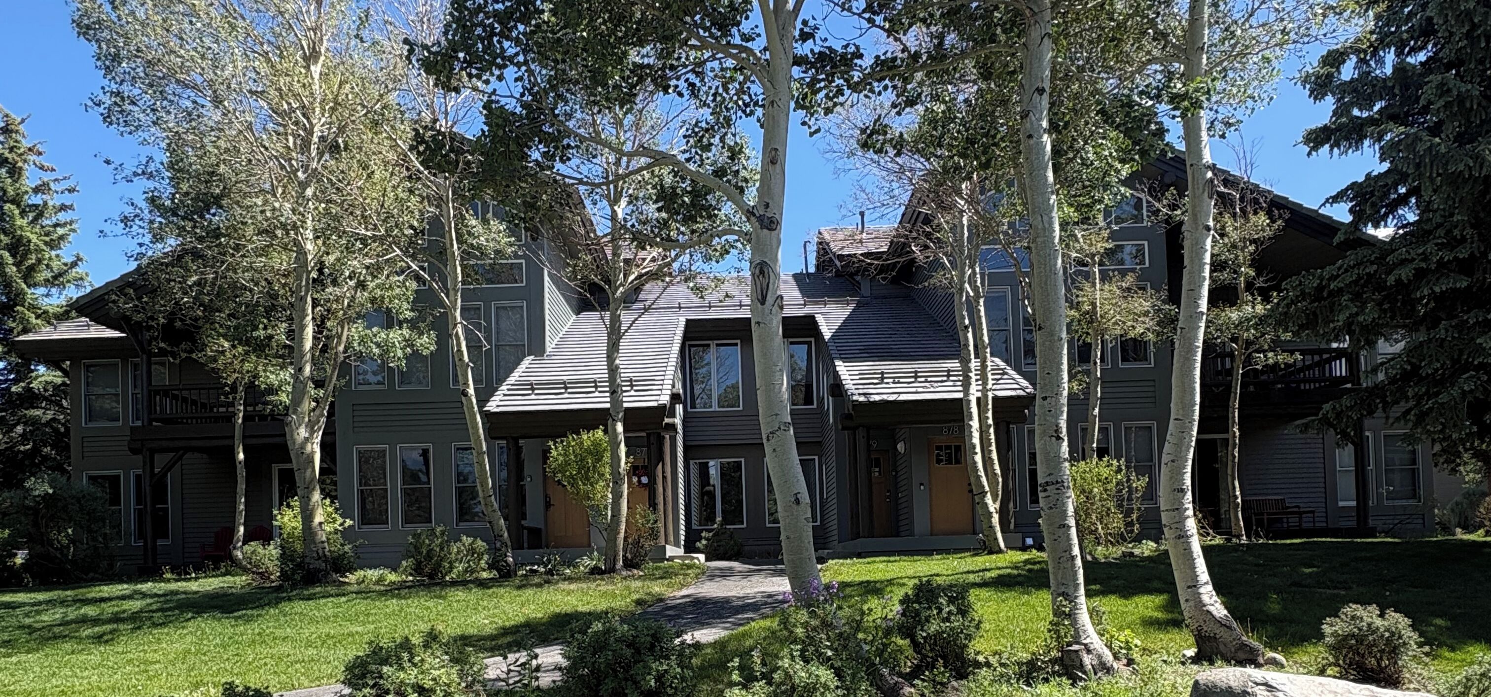 A multi-story residential building with a well-maintained lawn and mature trees.