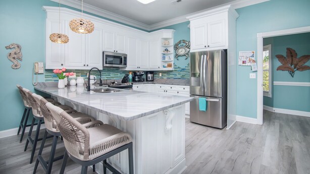 Una cocina moderna con muebles blancos, una isla central con taburetes de bar, un refrigerador de acero inoxidable y una lámpara sobre la encimera.