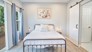 Un dormitorio con cama, mesita de noche, una obra de arte en la pared y una puerta corredera.