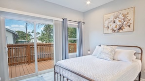 Un dormitorio con una cama grande, vistas a una terraza de madera y un cuadro en la pared.
