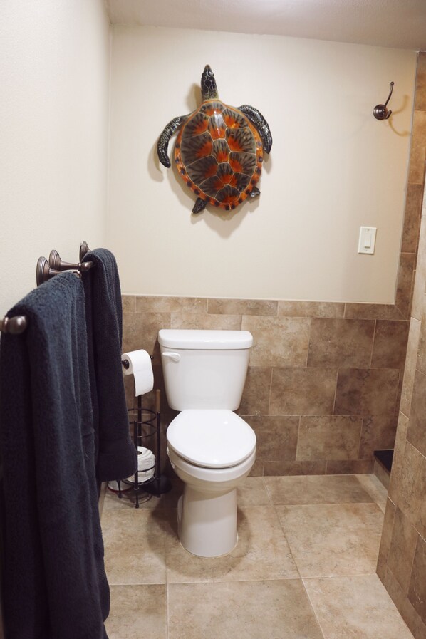 Un baño con inodoro, un perchero con una toalla oscura y un adorno de caparazón de tortuga en la pared.