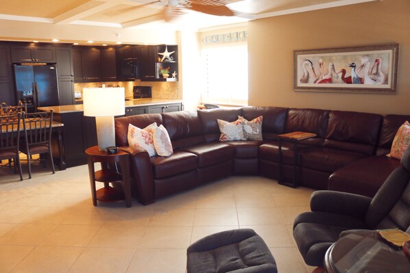 A modern living room with a sectional sofa, a dining area with chairs, and a kitchen in the background.