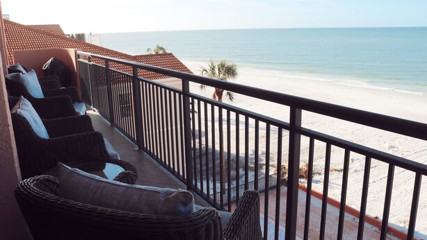 A balcony with wicker furniture overlooking a beach.