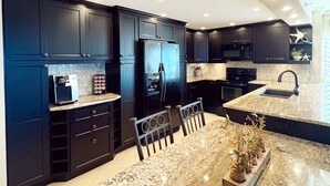 A modern kitchen with dark cabinetry, a granite countertop, and a central island with seating.