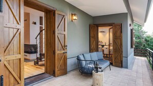 Un balcon spacieux avec une porte en bois donnant sur une cuisine, un canapé bleu et une petite table en bois sur laquelle se trouvent une bouteille et des verres.