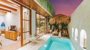 A modern outdoor pool area with a wooden deck, lounge chairs, and a thatched roof structure.
