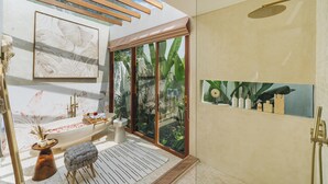 A modern bathroom with a freestanding bathtub, a shower area, and a large window with a view of greenery.