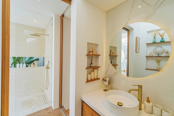 Une salle de bain moderne avec une douche à parois de verre, un miroir rond et des accessoires aux motifs de marbre.