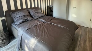 Een moderne slaapkamer met een gestreepte wand, een bed met grijze beddengoed, een kledingkast en een plafondlamp.