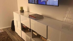 Een moderne woonkamer met een flatscreen televisie aan de muur, een witte tv-kast eronder en een houten vloer.