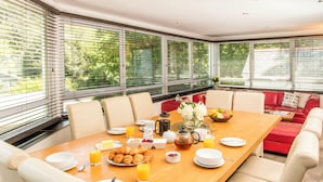 A dining area with a wooden table set for breakfast, including croissants, fruit, and beverages. - Large home. Close to Beach, all en-suite bedrooms. Peaceful Wooded valley views (St Agnes)