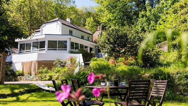 A house with a large garden, a patio with chairs, and a table. - Large home. Close to Beach, all en-suite bedrooms. Peaceful Wooded valley views (St Agnes)