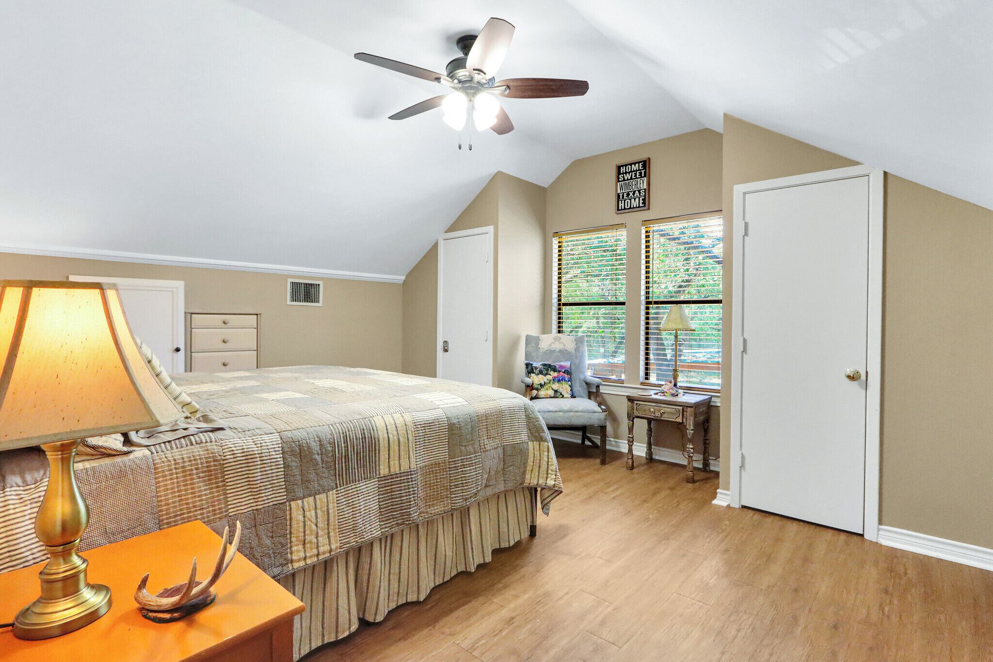 Une chambre à coucher comprenant un lit, un bureau, une chaise, un ventilateur de plafond et une fenêtre avec des stores.