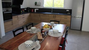 A modern kitchen with wooden cabinets, a dining table set with white and black patterned bowls, a fruit bowl, and a coffee maker.