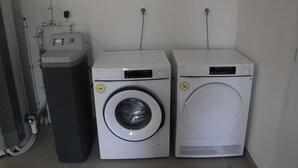 Two front-loading washing machines and a tall appliance, likely a dryer, in a laundry room with a tiled floor and white walls.