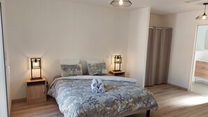A bedroom with a large bed, two bedside tables with lamps, a wooden wardrobe, and a bathroom with a shower curtain.