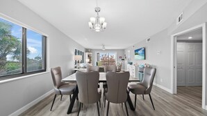 Une salle à manger moderne avec une grande table et six chaises, un lustre et une vue sur l’extérieur.
