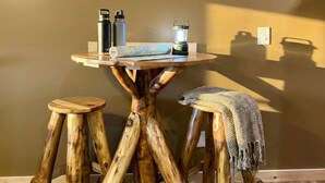 A rustic wooden table with stools, a framed landscape painting, and outdoor gear on the wall. - The Lake George Inn (Lake George)