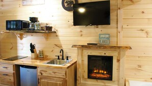 A wooden interior with a kitchen area featuring a microwave, coffee maker, sink, and a flat-screen TV mounted on the wall. - The Lake George Inn (Lake George)
