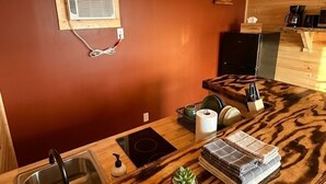 A kitchen with a wooden countertop, a sink, a window, and a small plant. - The Lake George Inn (Lake George)