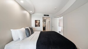 Una habitación de hotel moderna con una cama grande, paredes blancas y una colcha acolchada negra.