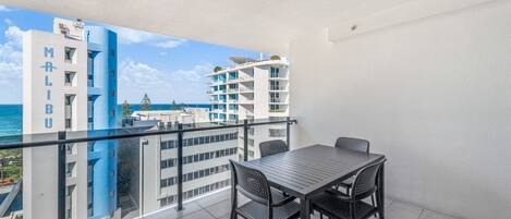 A balcony with a table and chairs, overlooking a cityscape with modern buildings and a view of the sea.