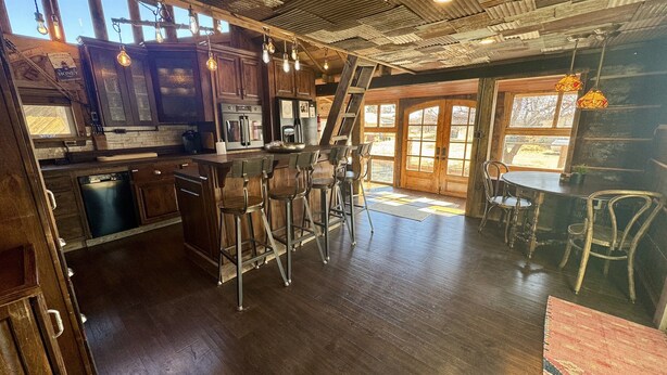 Een landelijke keuken met houten kasten, een roestvrijstalen koelkast en een bar voorzien van krukken.