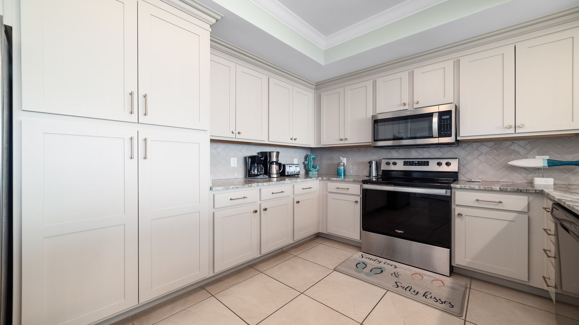 Een moderne keuken met witte kasten, roestvrijstalen apparatuur en een backsplash van herringbone tegels.