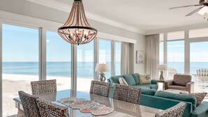 A spacious room with a large window overlooking the beach, a chandelier, and a teal sofa. - 4BR Beachfront, Lazy River w/ Slide, New to Market!! (Orange Beach)
