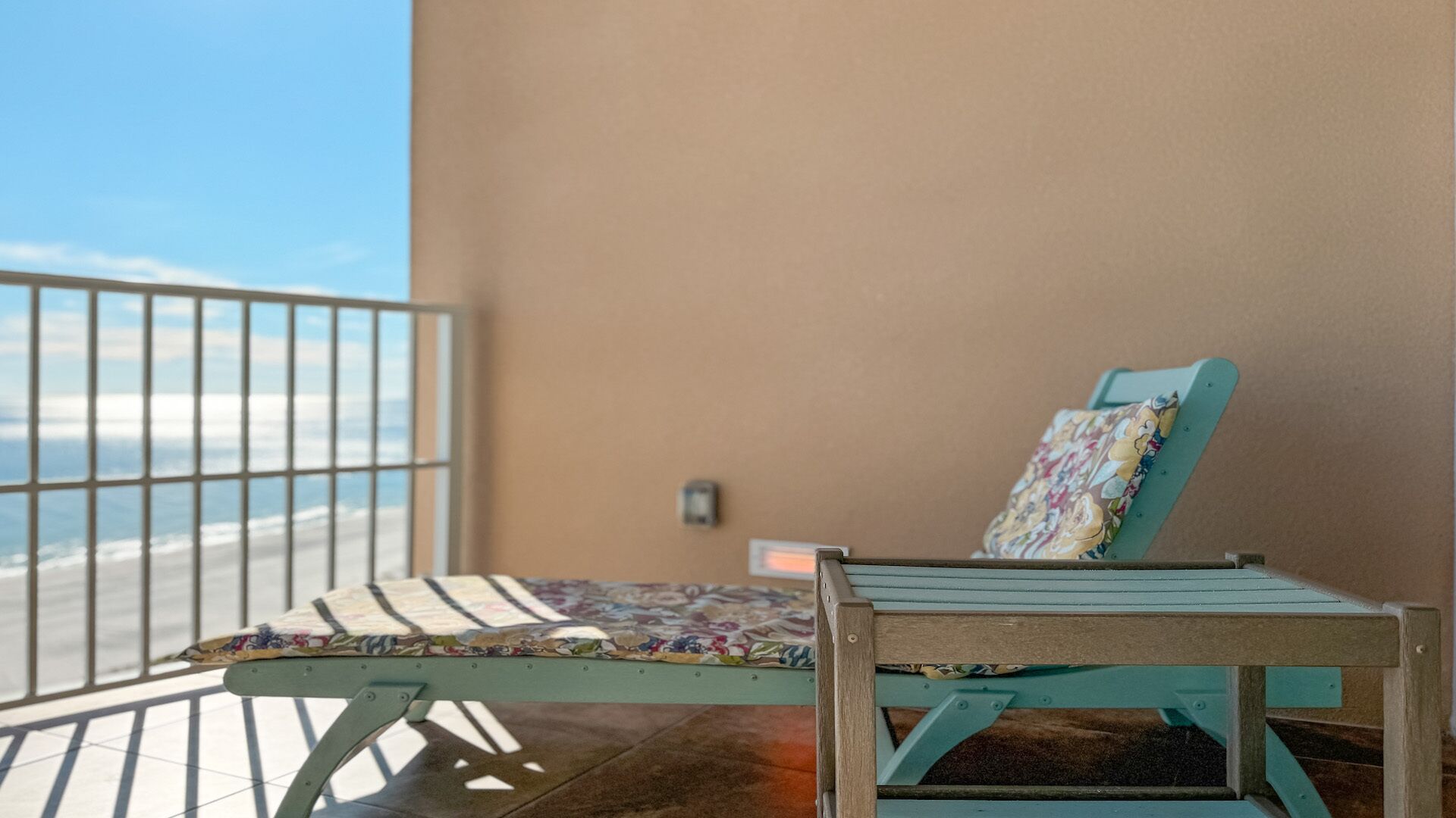 A balcony with a chair and a small table, overlooking a beach.