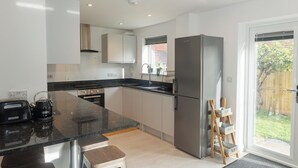 Een moderne keuken met een zwart aanrecht, roestvrijstalen apparatuur en een schuifdeur naar een achtertuin.