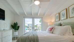 A bedroom with a bed, a nightstand, a dresser, a plant, and a view of the outside. - Flamingo Bay~ Pool, Cabana Club, 30' Dock! (Key Colony Beach)