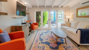 A spacious living area with a large TV, orange chairs, a white sofa, and a patterned rug. - Flamingo Bay~ Pool, Cabana Club, 30' Dock! (Key Colony Beach)