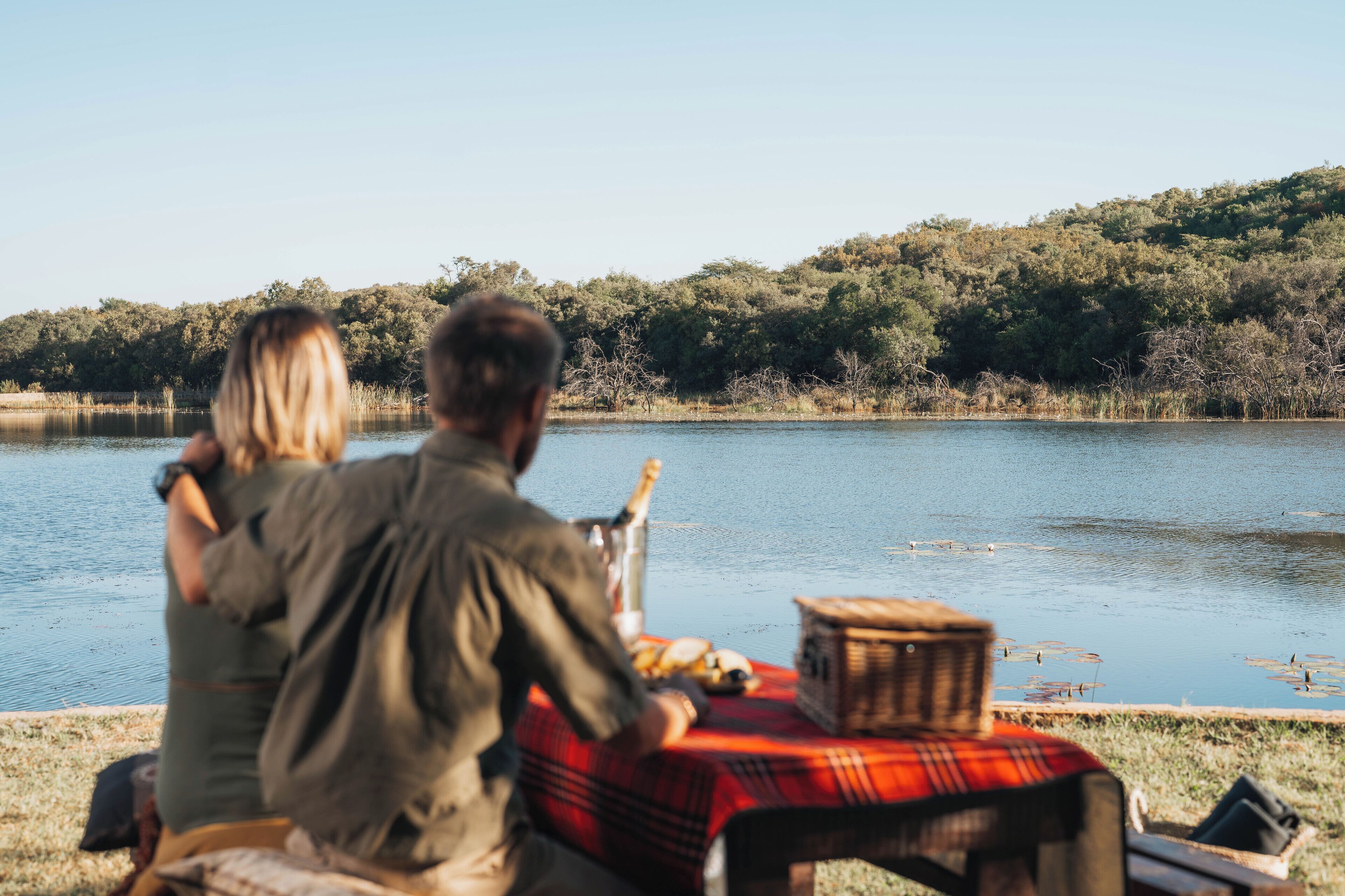 A couple sitting at a table by a lake with a picnic setup.