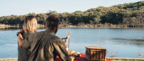 A couple sitting at a table by a lake with a picnic setup.