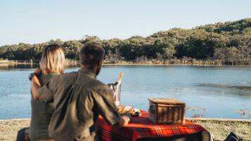 A couple sitting at a table by a lake with a picnic setup.