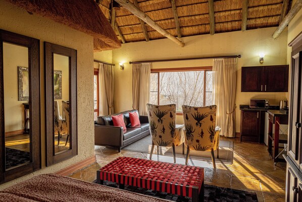 A room with a sofa, two chairs, a red woven bench, a large mirror, and a kitchen area. - Room in Guest Room - Mmakuba Private Game Lodge, Deluxe Chalet 9A (Mookgopong)