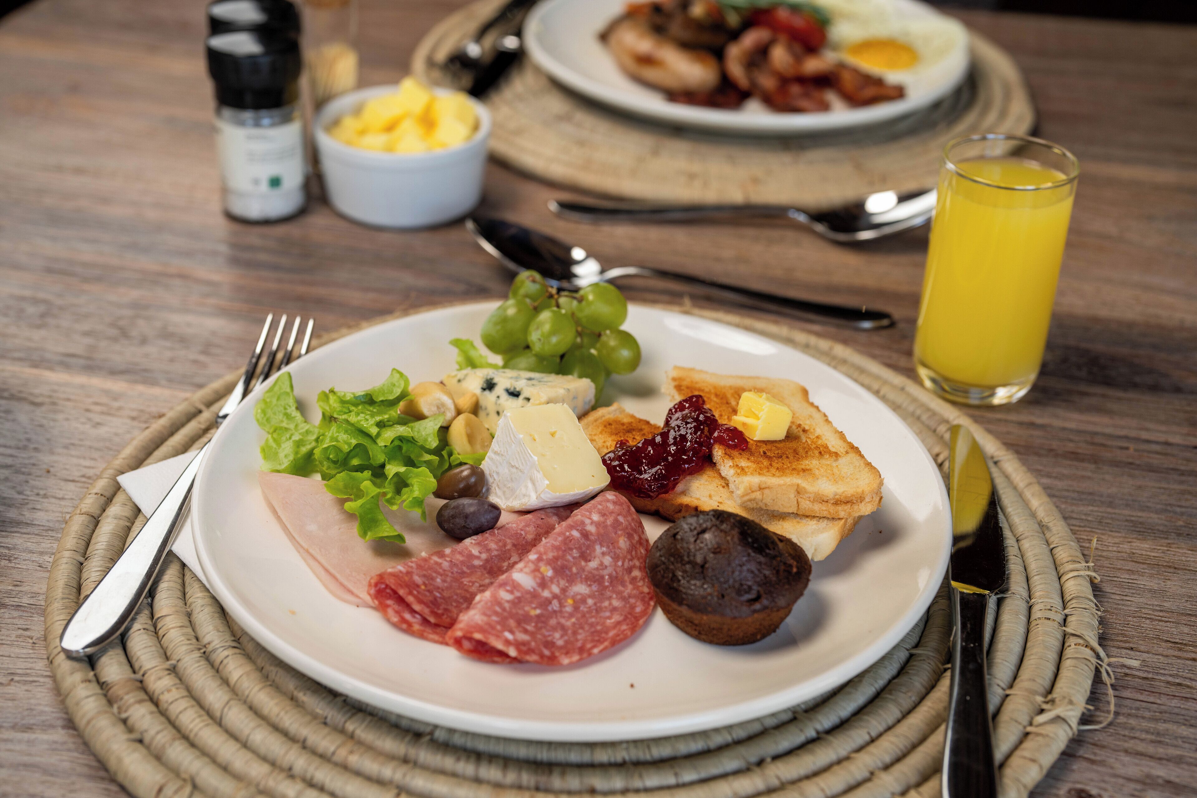 A breakfast plate with various foods, a glass of orange juice, and dining utensils on a wooden table.