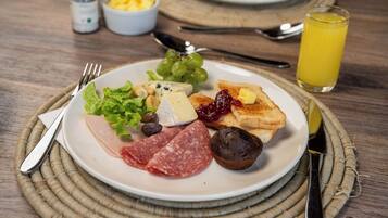 Un plato de desayuno con diferentes alimentos, un vaso de jugo de naranja y cubiertos sobre una mesa de madera.