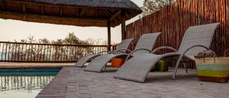 A poolside area with lounge chairs and a thatched roof structure.
