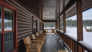Eine überdachte Holzterrasse mit Bänken, großen Fenstern und Blick auf eine verschneite Landschaft.