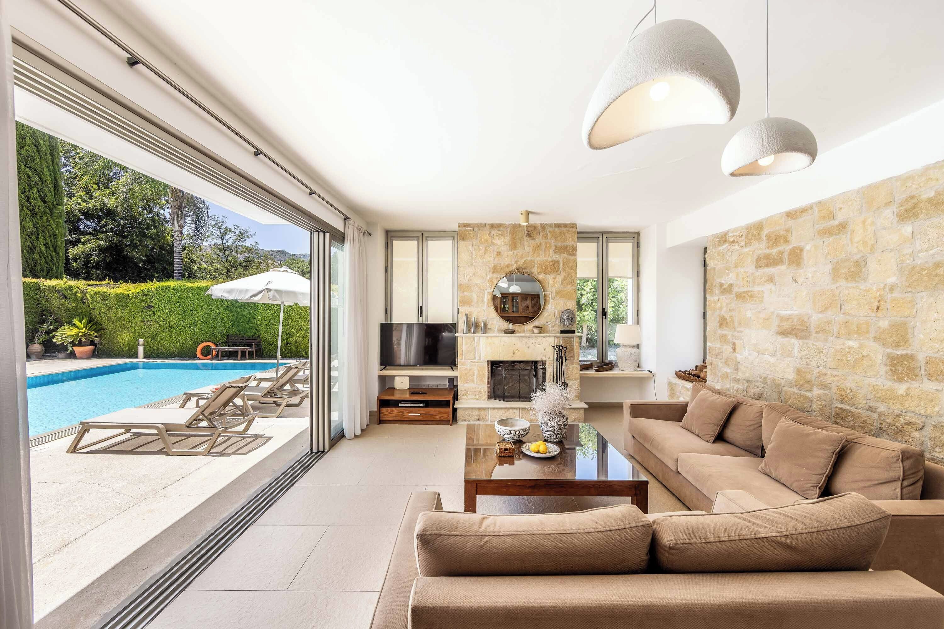 A modern living room with a stone fireplace, a television, and a pool view.